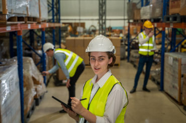 Warehouse employees reading a clipboard in a logistics centre,Warehouse worker taking packages for shipment in a large distribution centre.