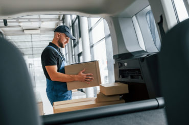 With vehicle. Delivery man in uniform is indoors with car and with order.